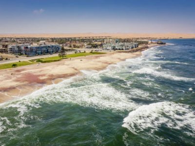 Swakopmund Promenade at the Beach and Coast along the South Atlantic Ocean under blue summer sky. Large Desert Dunes behind the Town of Swakopmund visible on the horizon. Aerial Drone Point of View, South Atlantic Ocean, Swakopmund, Erongo Region, Namibia, Africa.